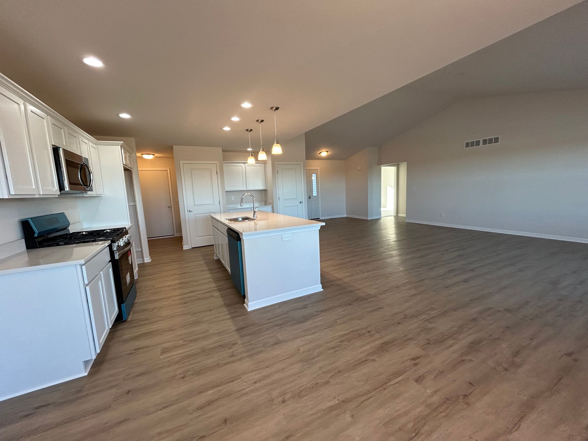 Modern kitchen with island, white cabinets, appliances, and wood-look flooring.