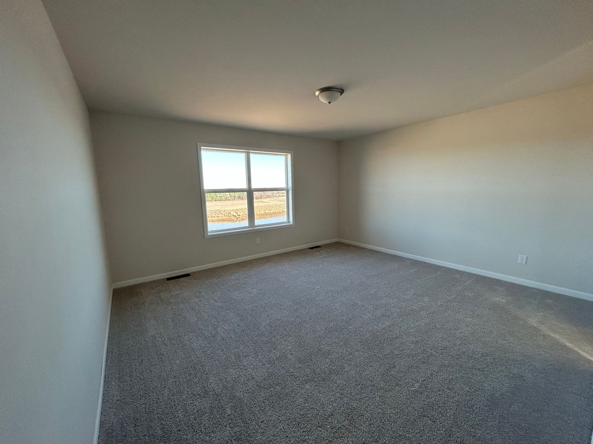 Empty room with gray carpet and walls, a window, and a ceiling light.