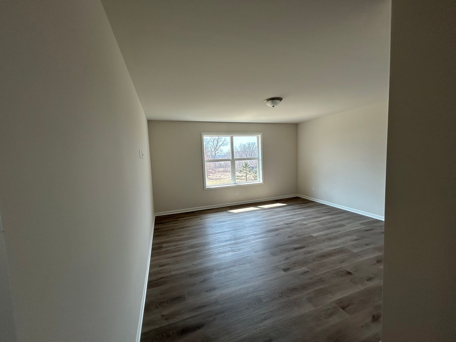 Empty room with wood-look flooring, a window, and white walls.