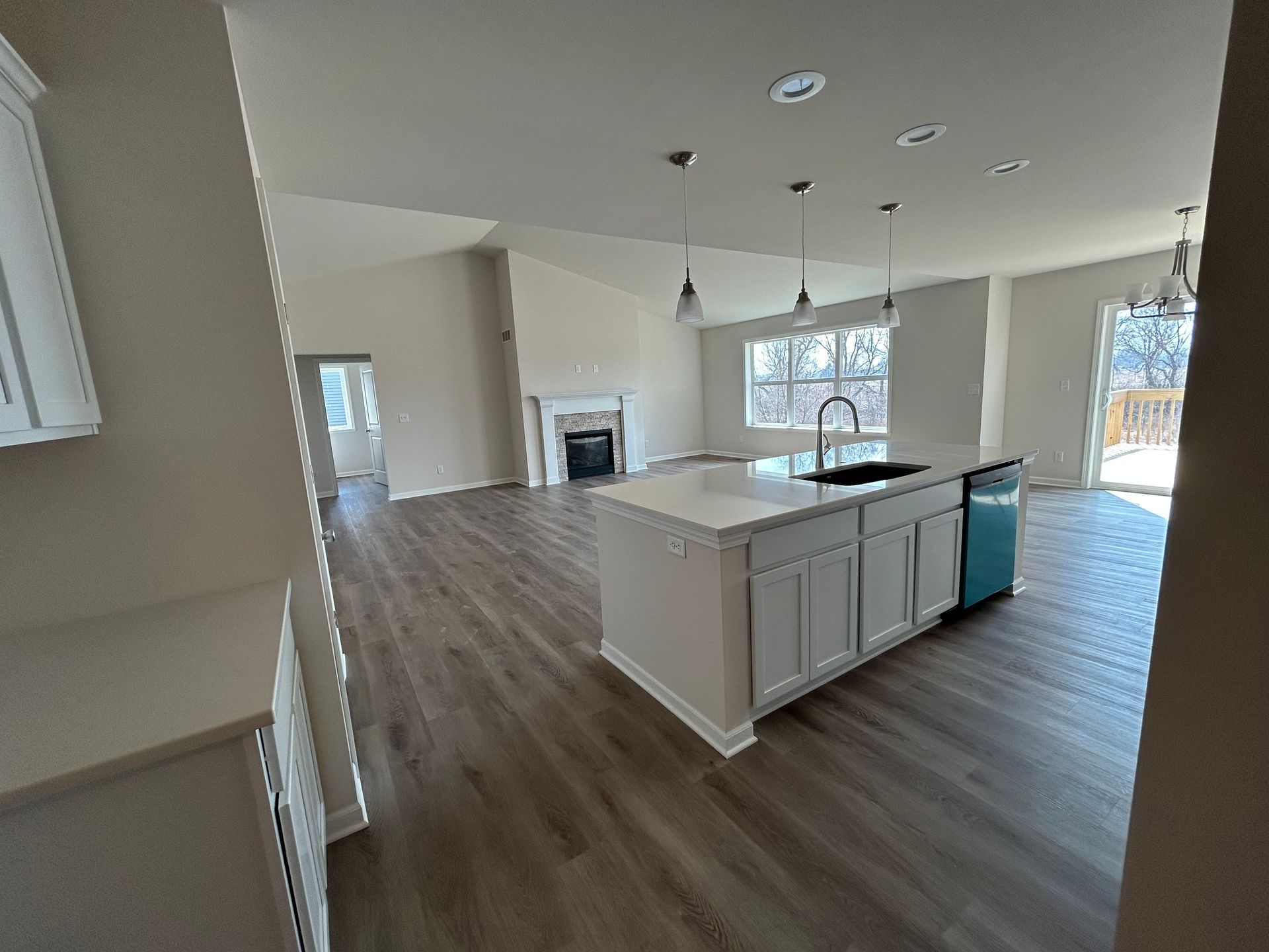 Open-concept kitchen with island, sink, and teal dishwasher. Living area with fireplace and windows.