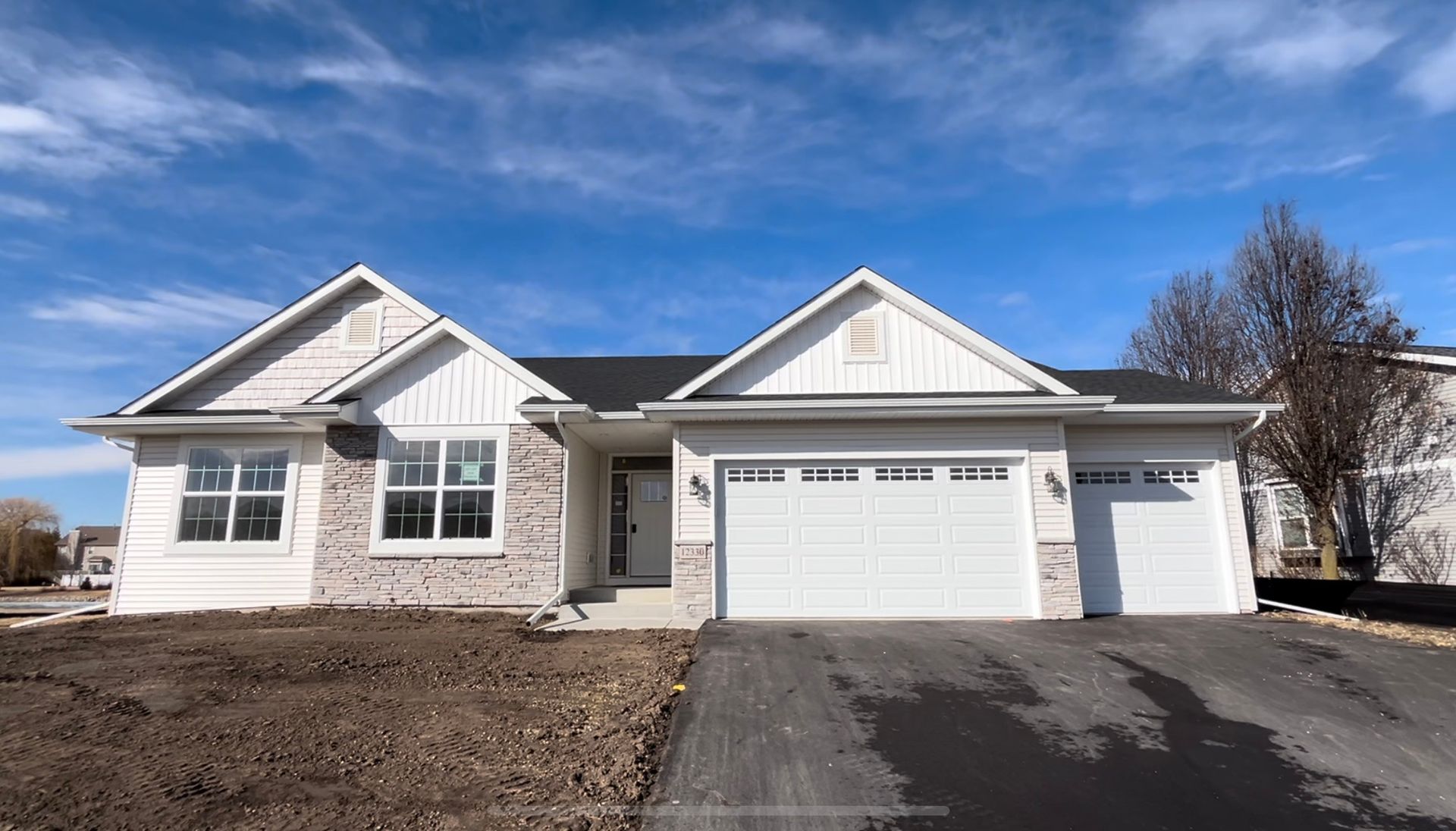 New single-story house with white siding, light gray brick, and a two-car garage under a blue sky.