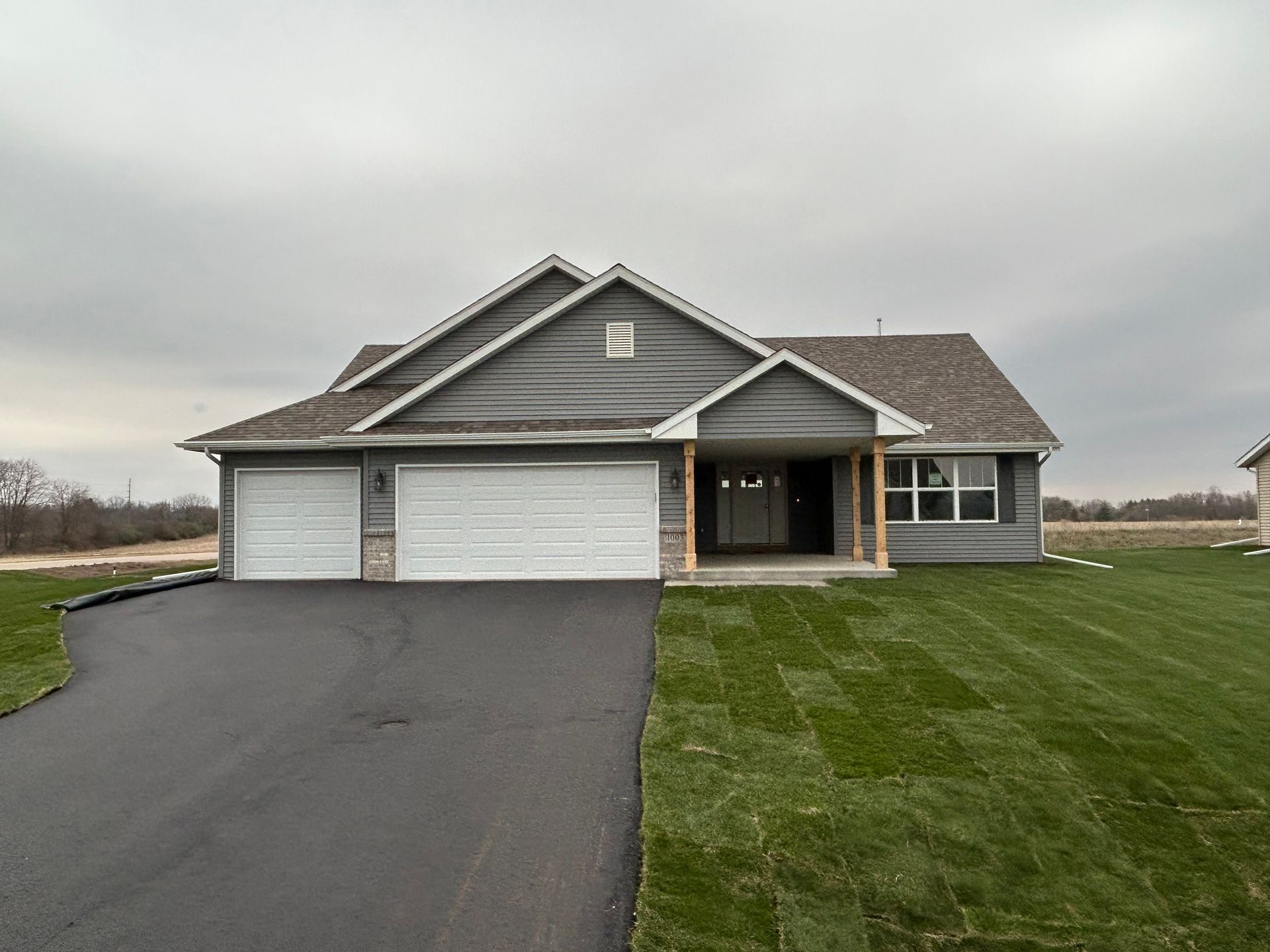 Gray-sided house with a two-car garage and porch, on a freshly sodded lawn, under an overcast sky.