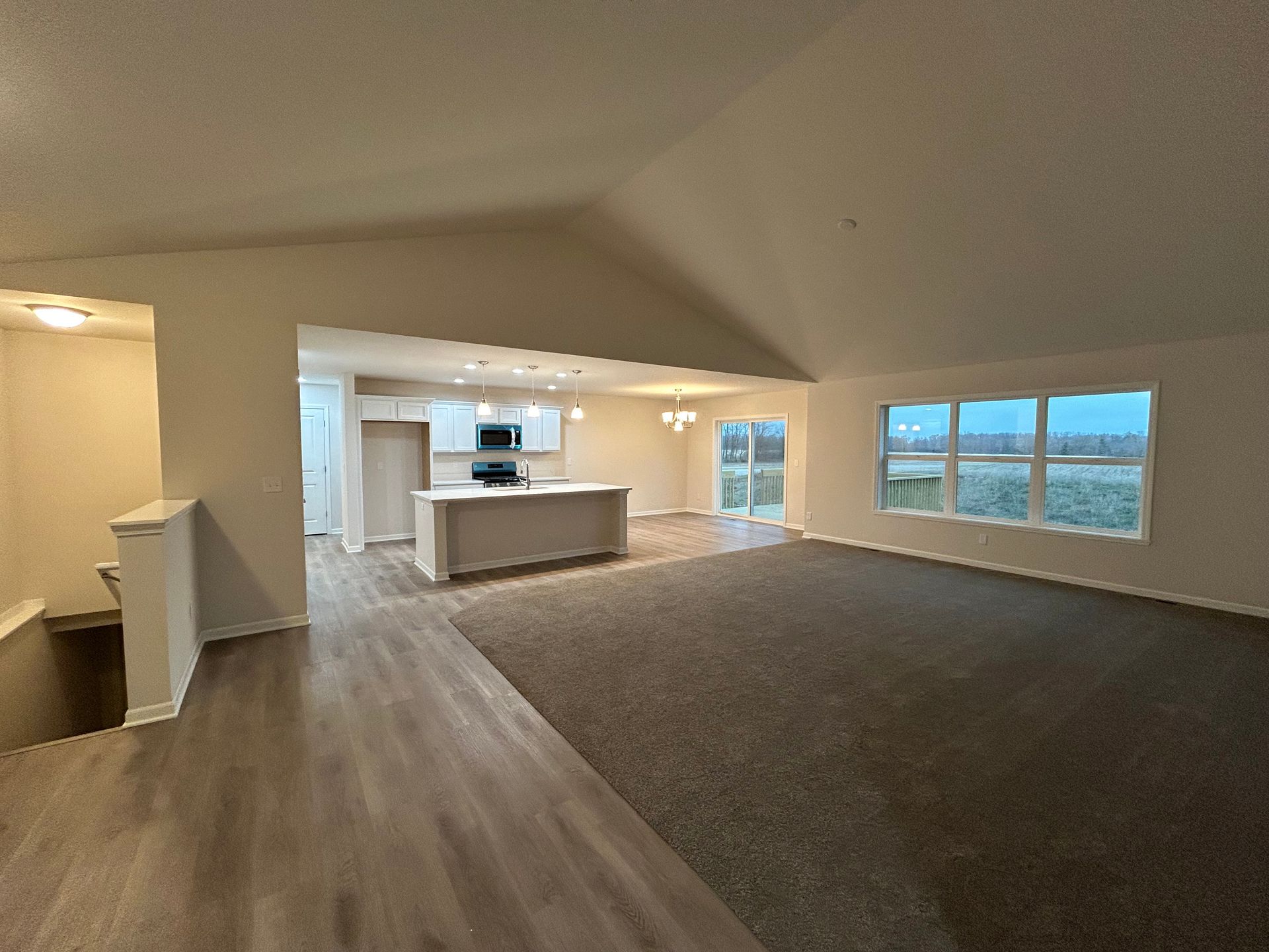 Spacious open-concept living area with kitchen. Tan walls, dark carpet, light island, and large windows.