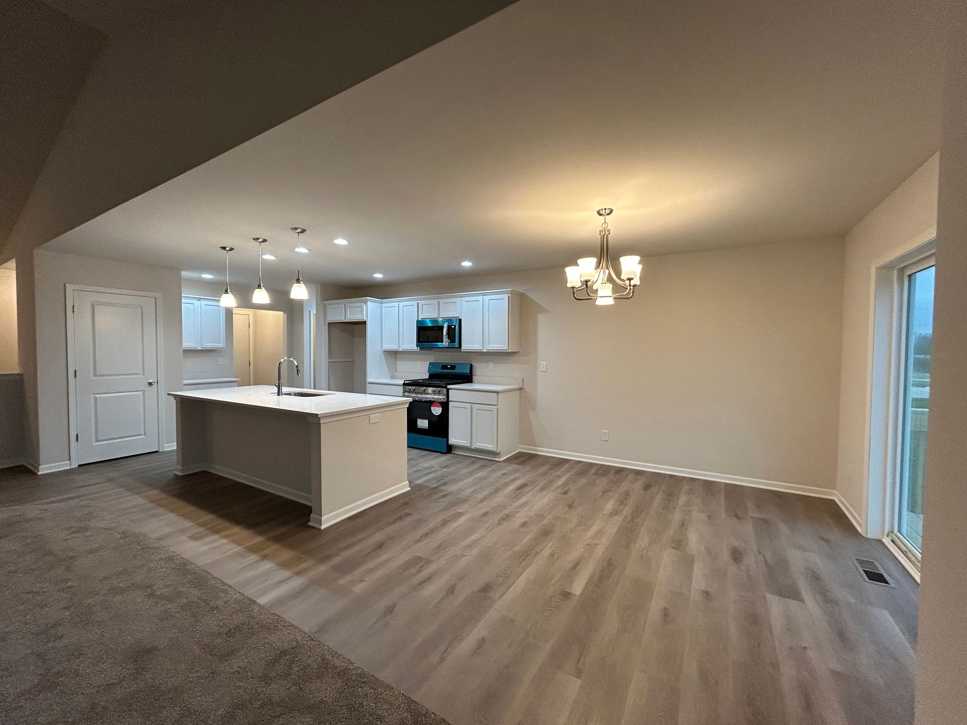 Open-concept kitchen with island, white cabinets, and light wood floors. Chandelier and sliding glass door.