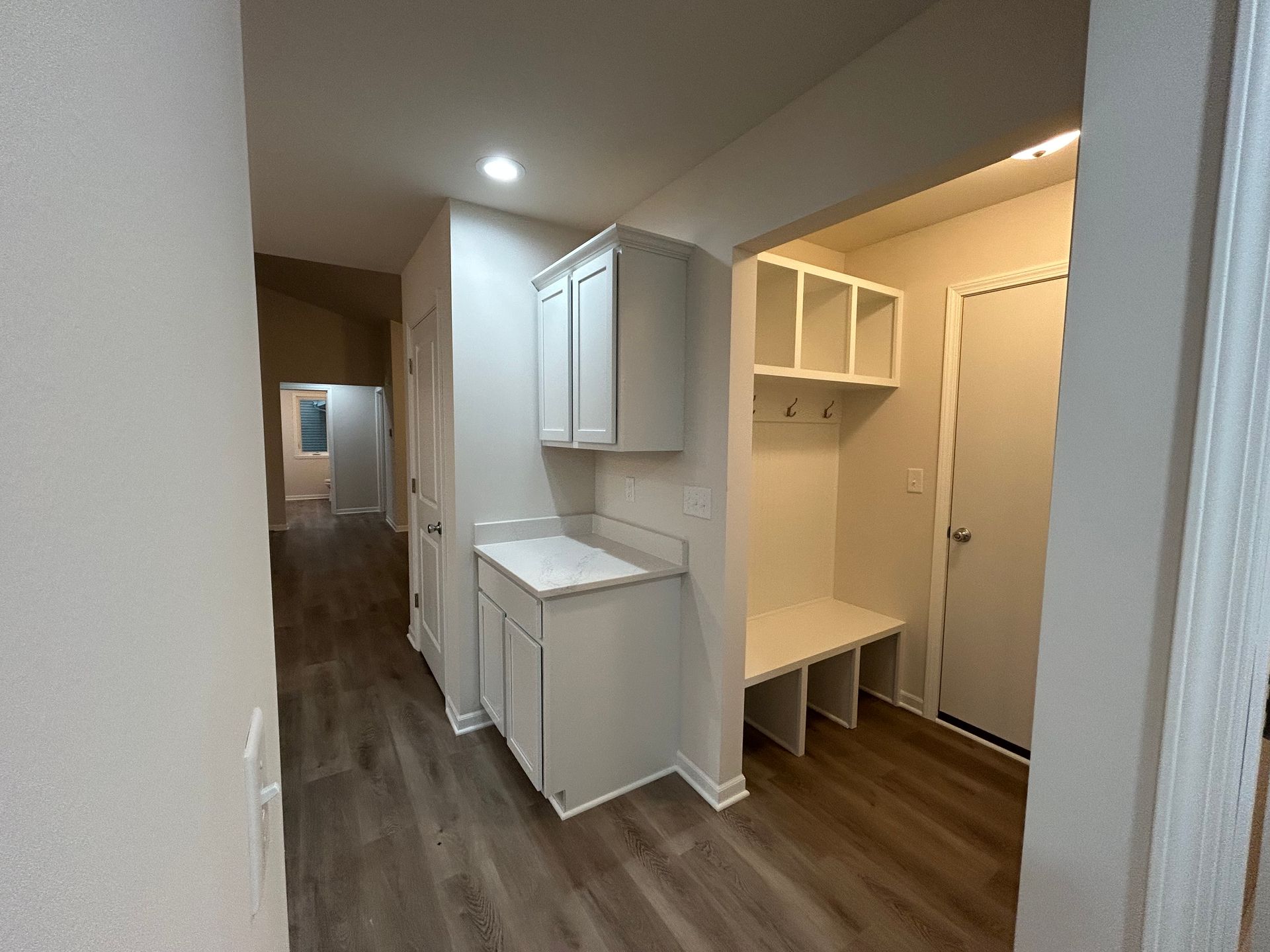 Hallway with white cabinets, built-in bench, and gray flooring. A door is visible at the end of the hall.