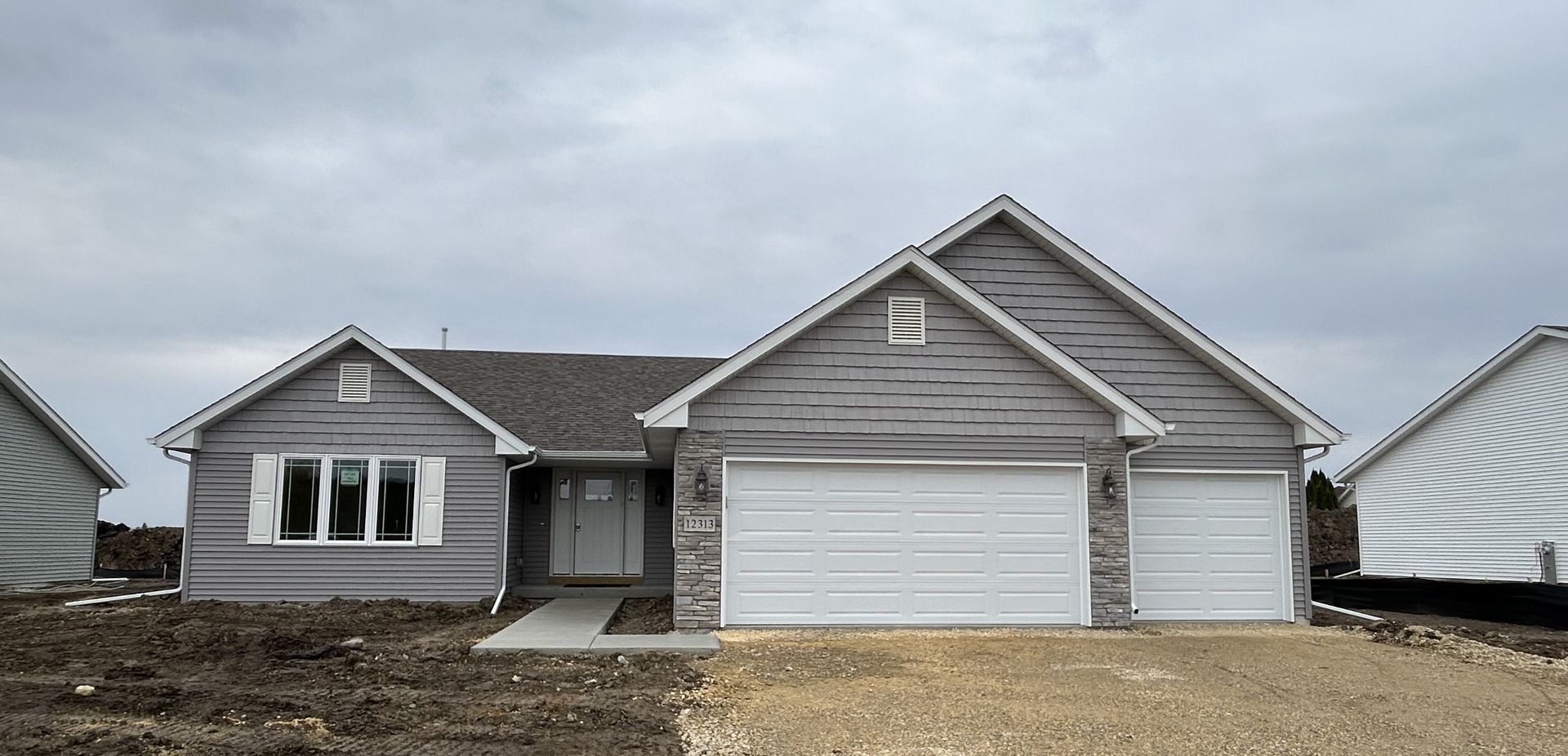 New house exterior under a cloudy sky. Gray siding, two-car garage, small front yard.