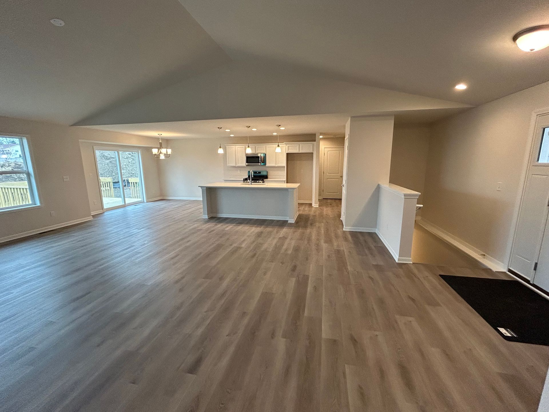 Open-concept living area with light wood floors, white kitchen island, and access to a patio.