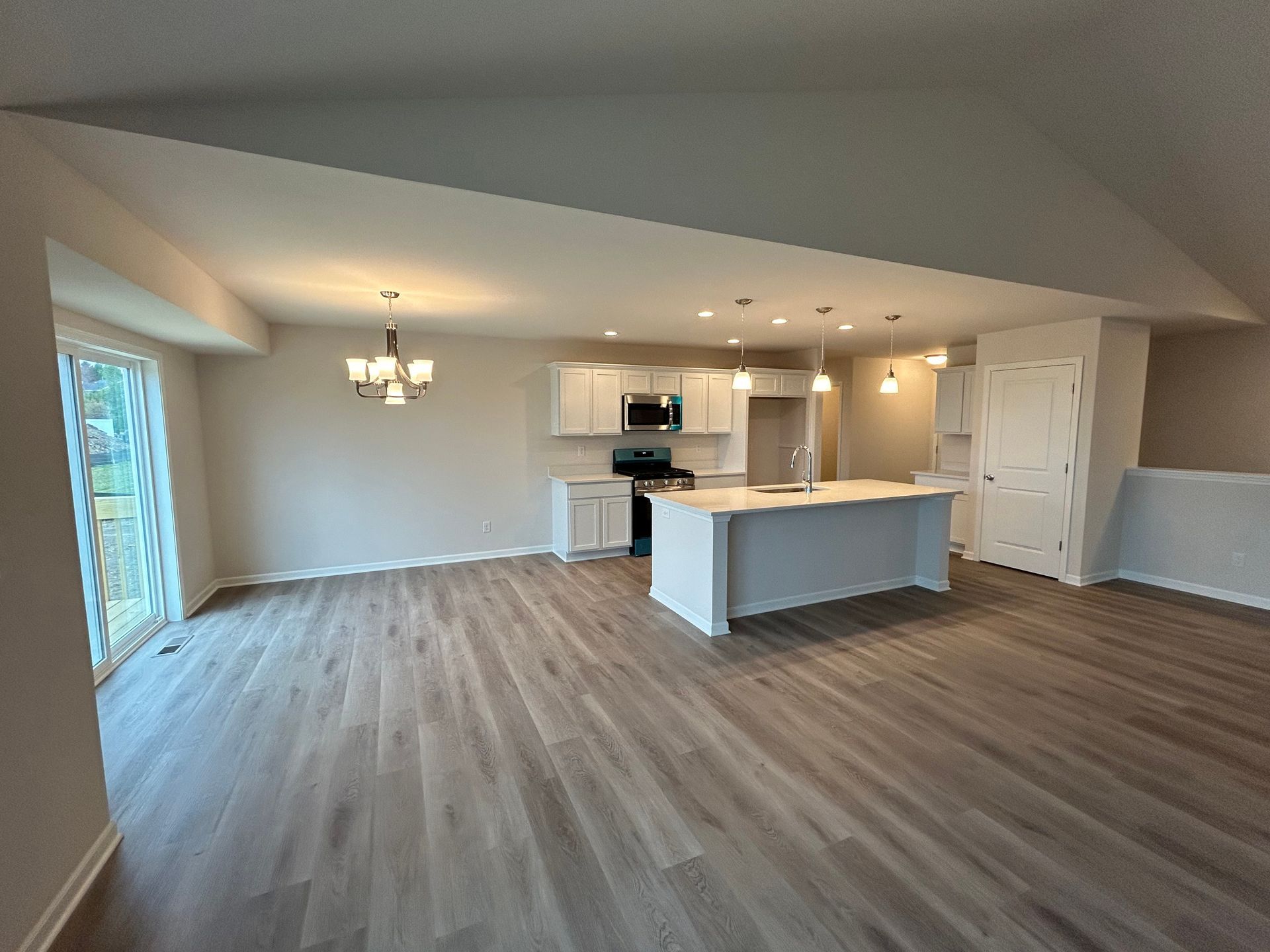 Open-concept kitchen and living area with white cabinets, island, and light gray wood flooring.