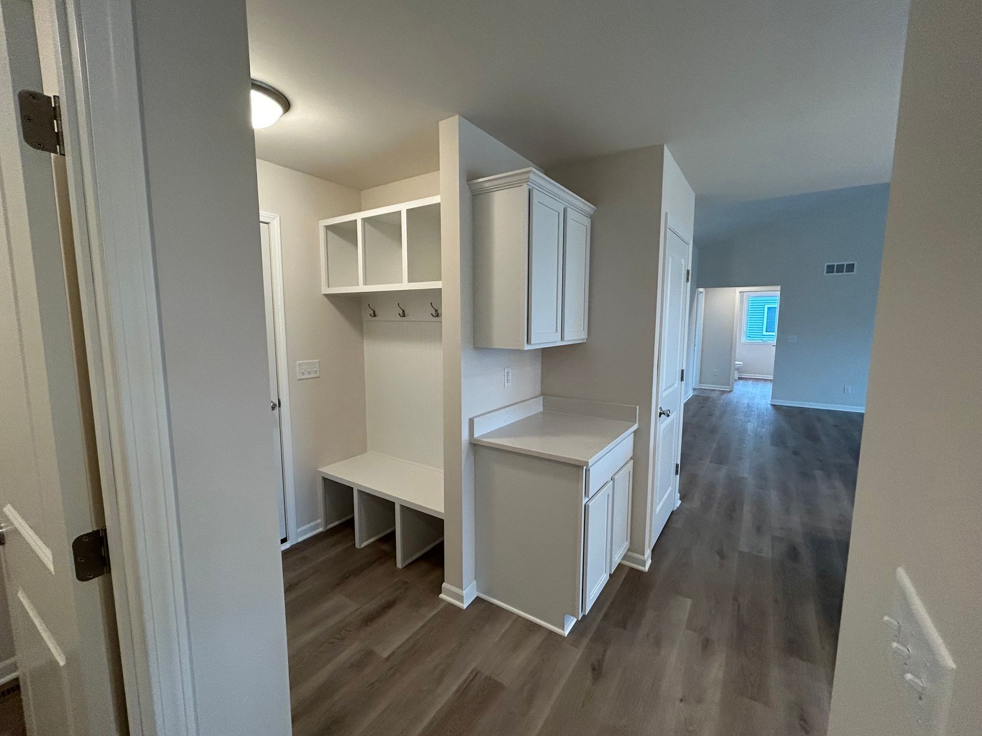 Mudroom with built-in storage, bench, and cabinets. Light gray walls and wood-look flooring.