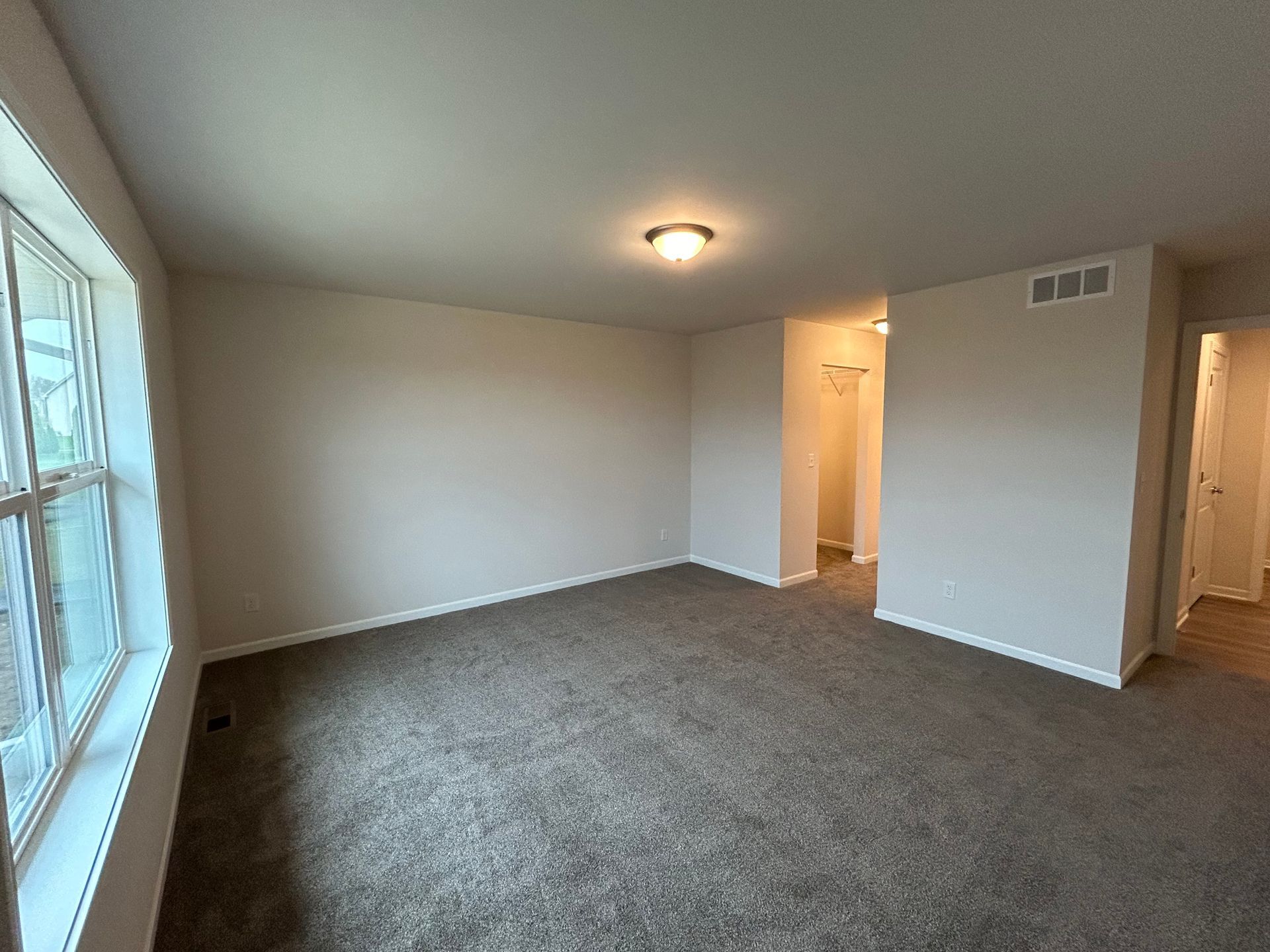 Empty bedroom with gray carpet, beige walls, and a window.