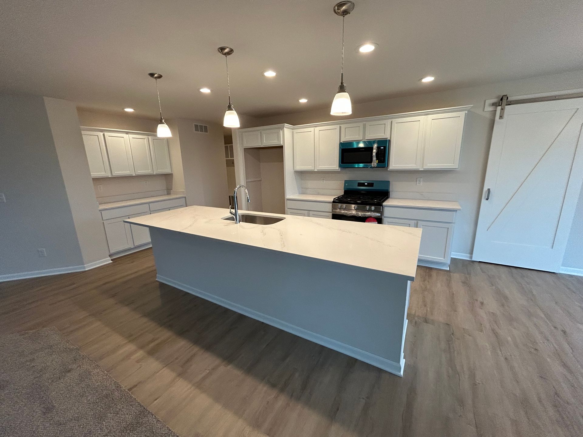 Modern kitchen with a large island, light cabinets, wood-look flooring, and stainless steel appliances.