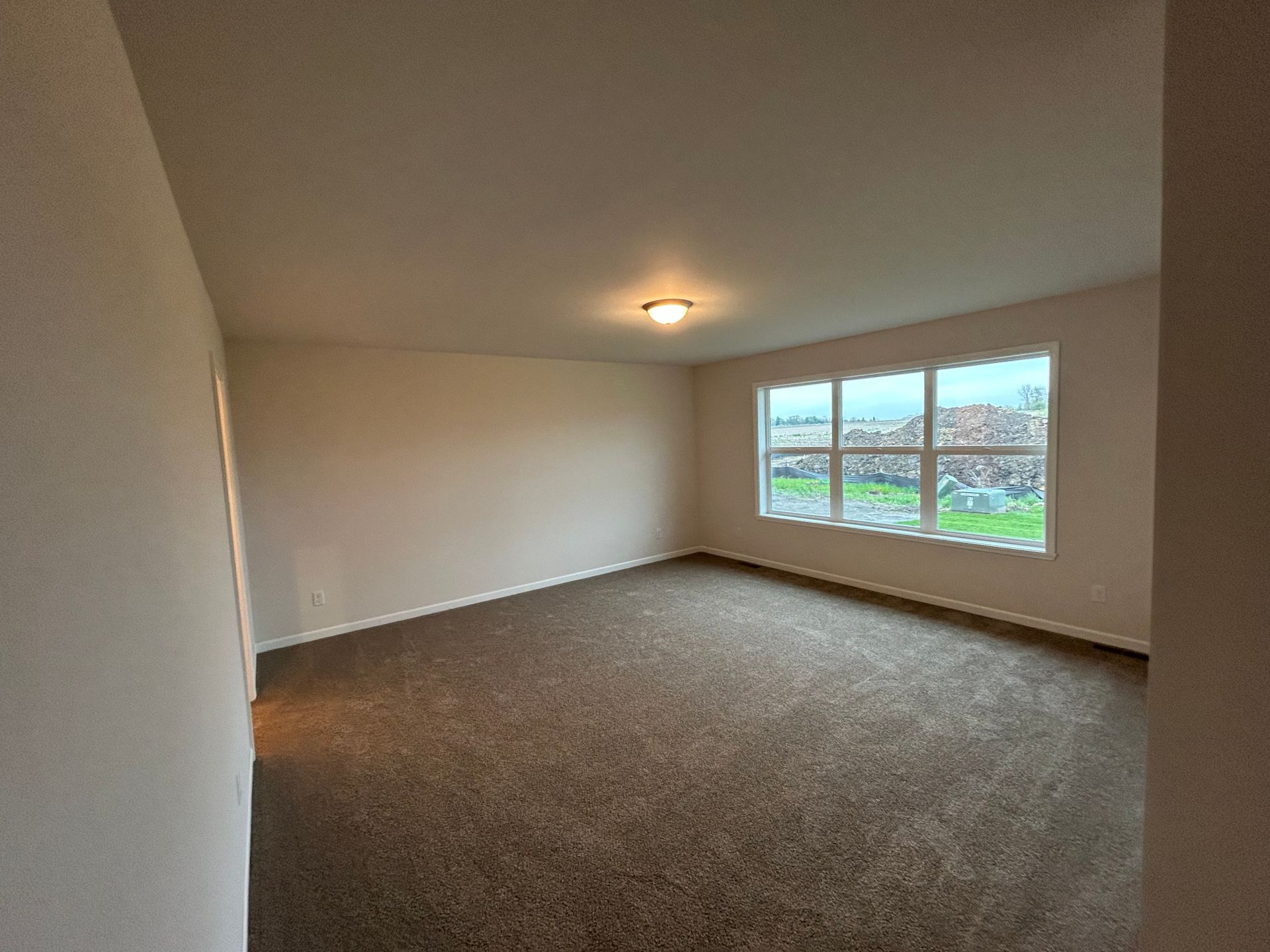 Empty room with brown carpet, white walls, and a window overlooking a green lawn.