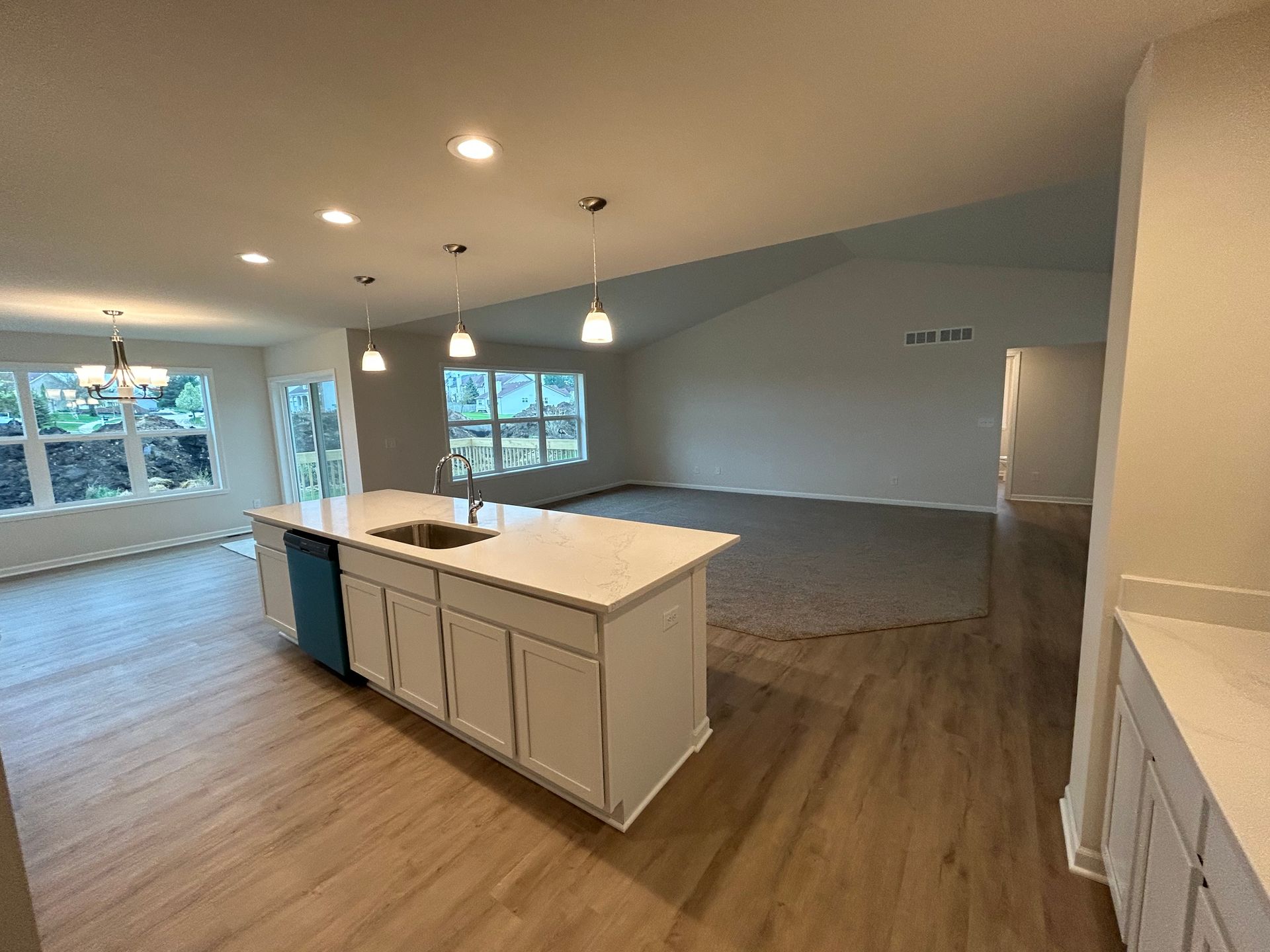 Open concept kitchen with island, cabinets, and light fixtures; living room with windows and high ceiling.