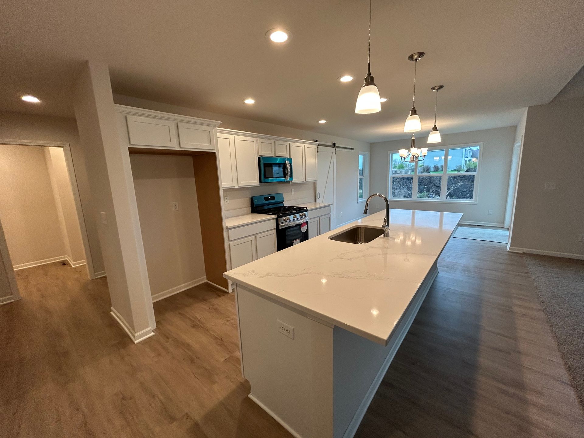 Modern kitchen with white island, cabinets, and appliances. Wooden floors and large windows.