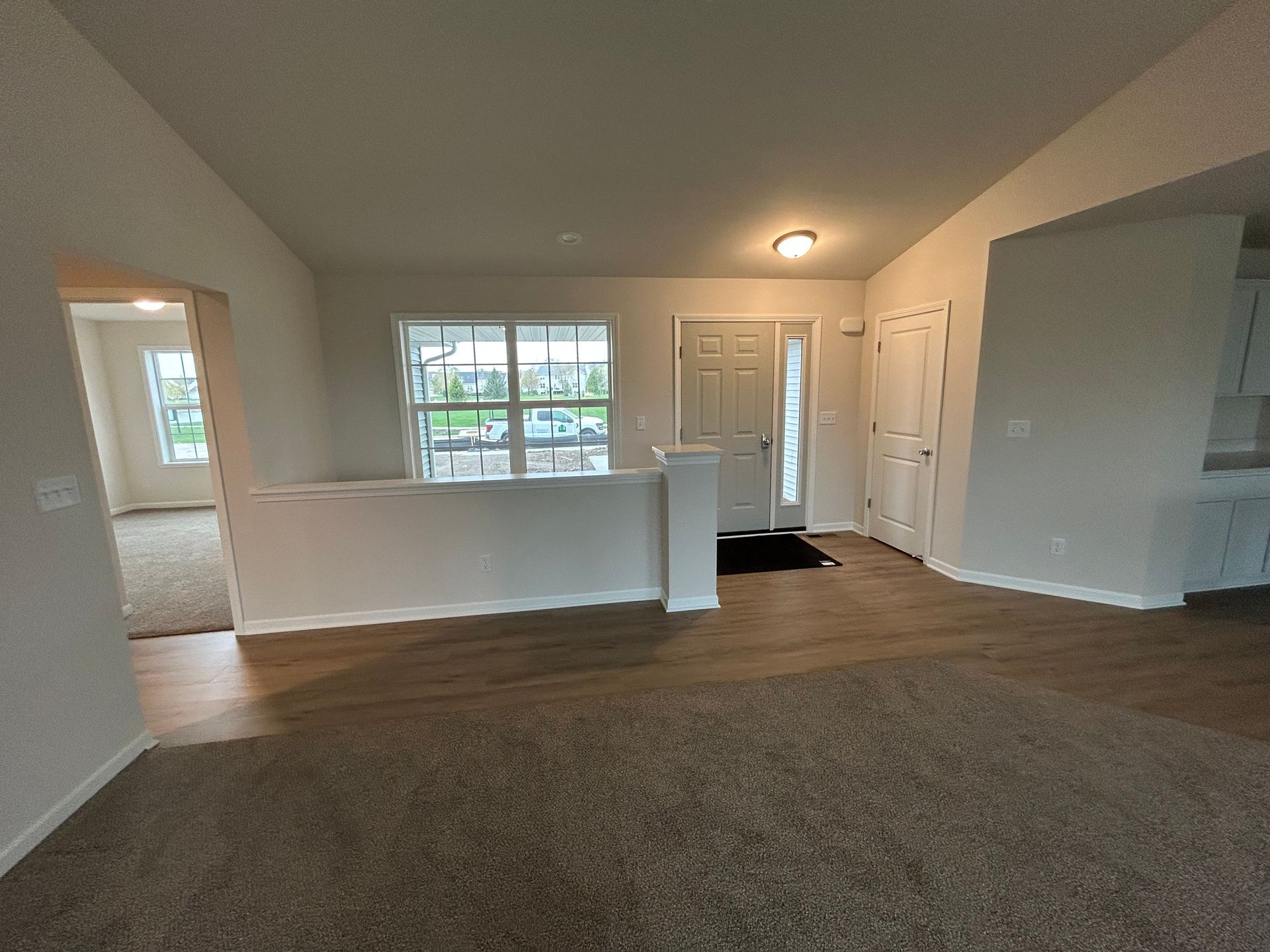 Living room with gray carpet and laminate flooring, a front door, and a half wall.