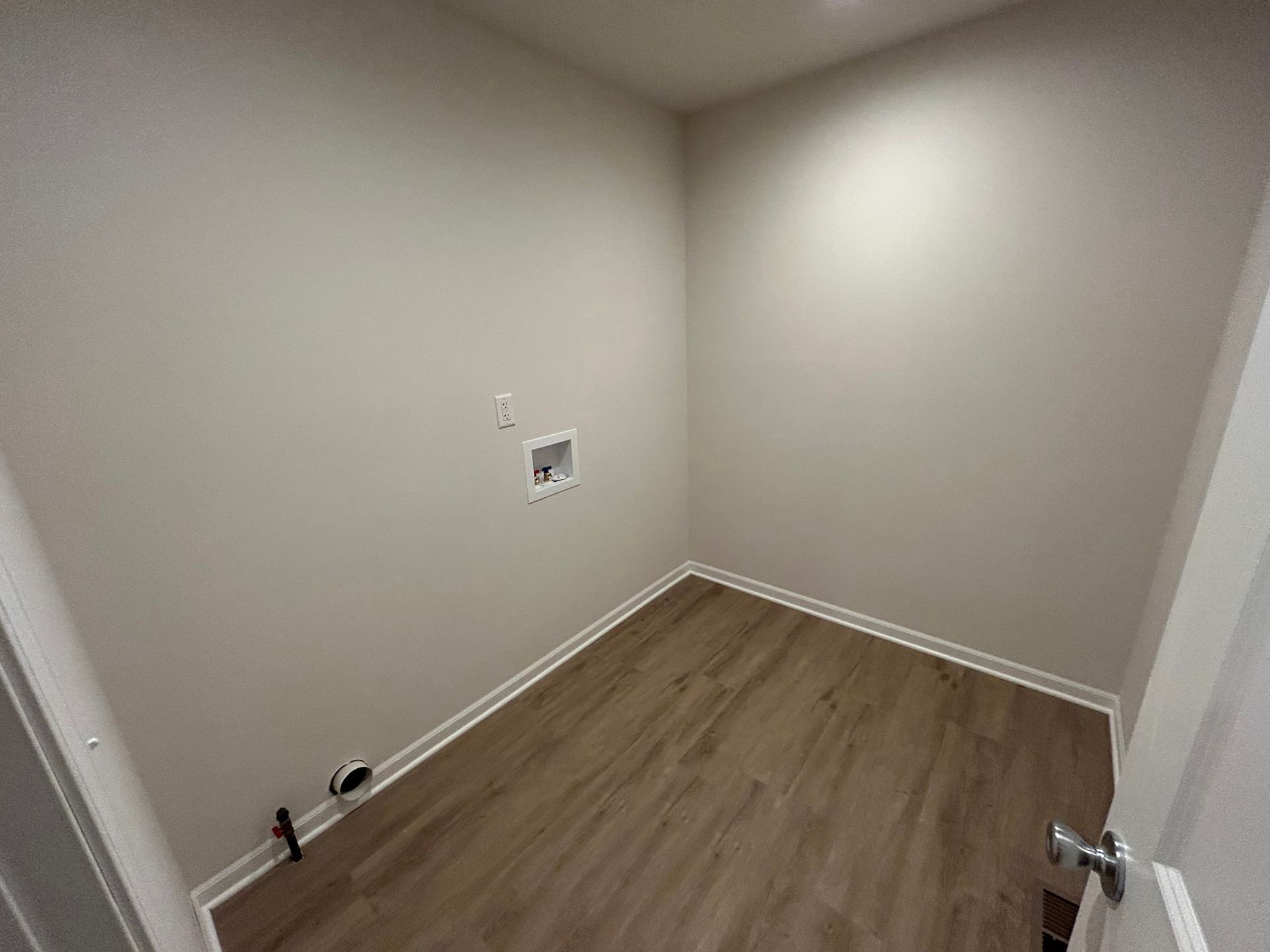 Empty laundry room with beige walls and wood-look flooring. Washer and dryer hookups visible.