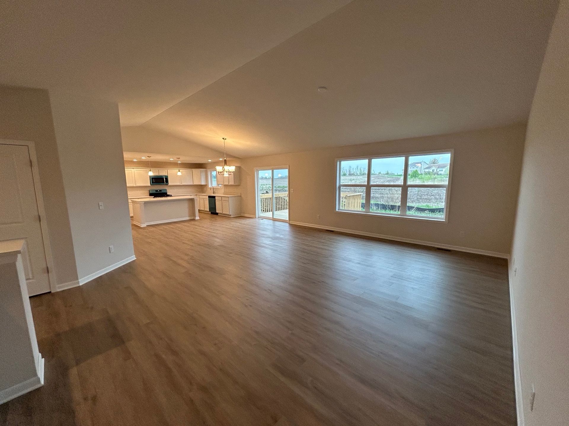 Open-concept living space with dark wood floors, kitchen, and windows. Beige walls and white cabinets.