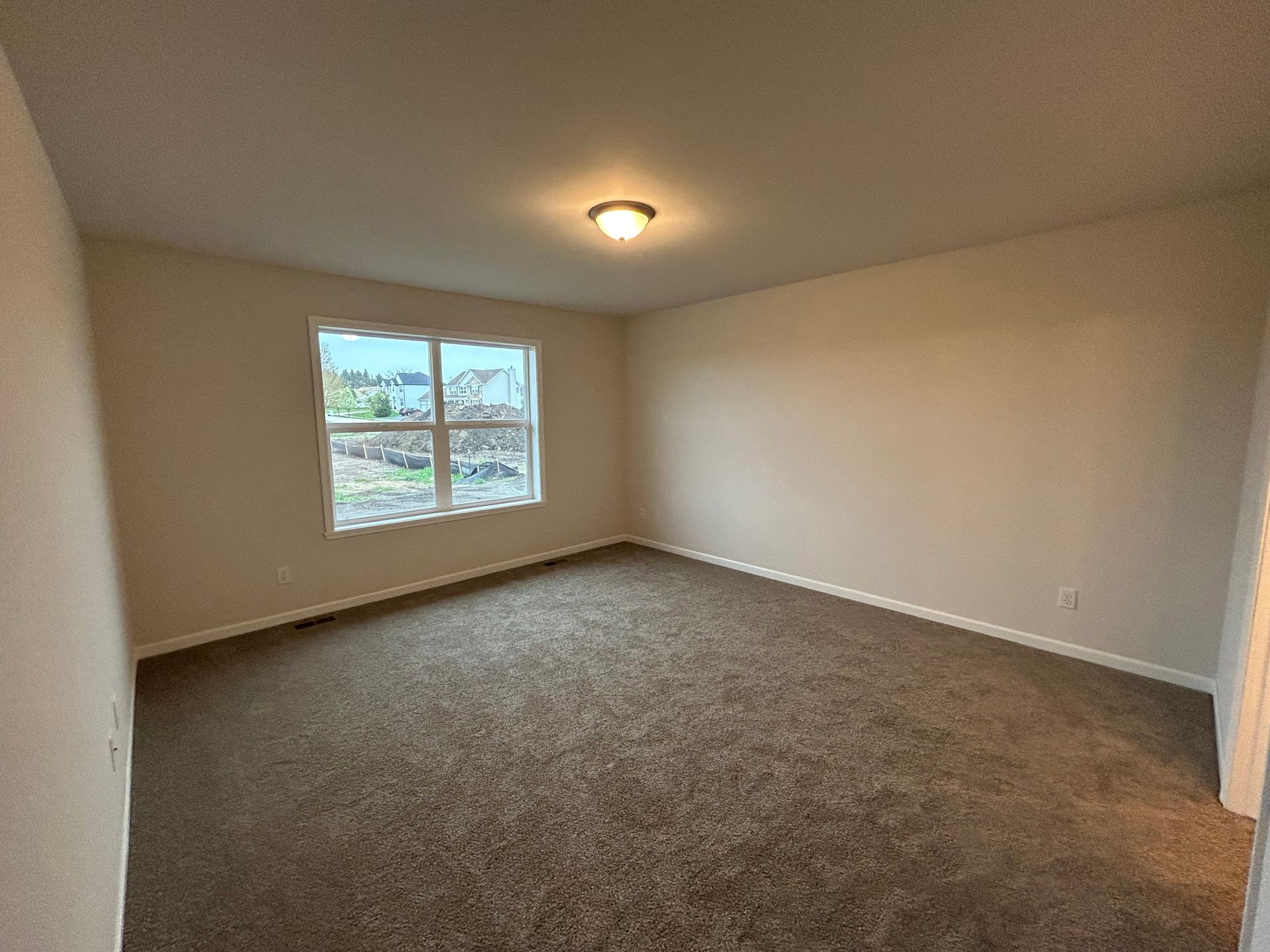 Empty bedroom with brown carpet, a window, and tan walls.