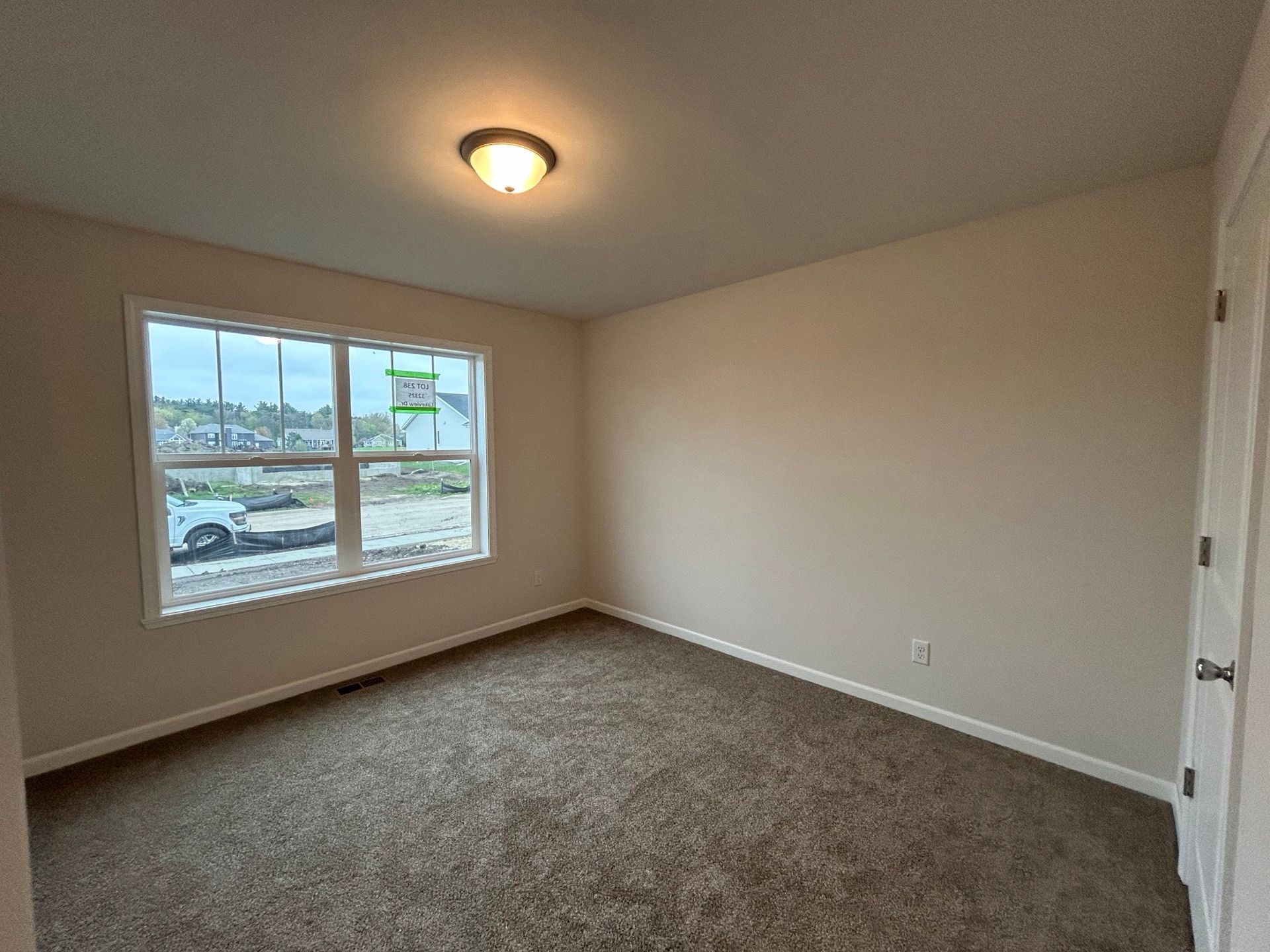 Empty beige bedroom with a window, a door, and brown carpet.