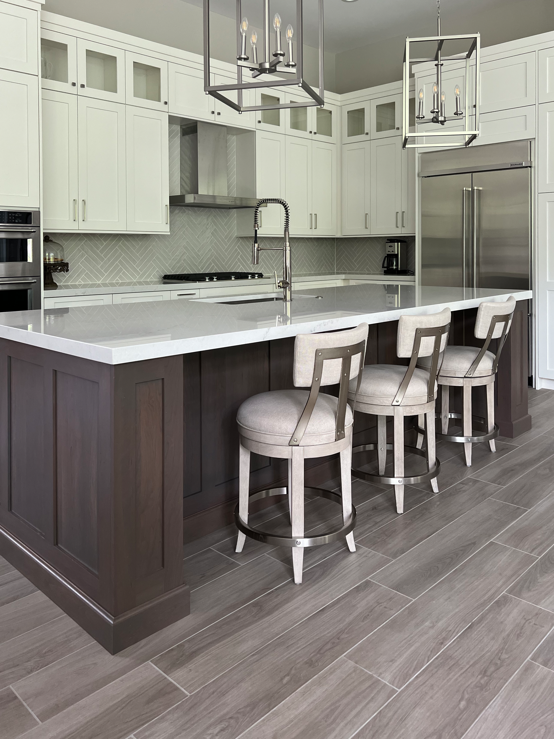 Modern kitchen with white and gray cabinets, island with stools, and stainless steel appliances.