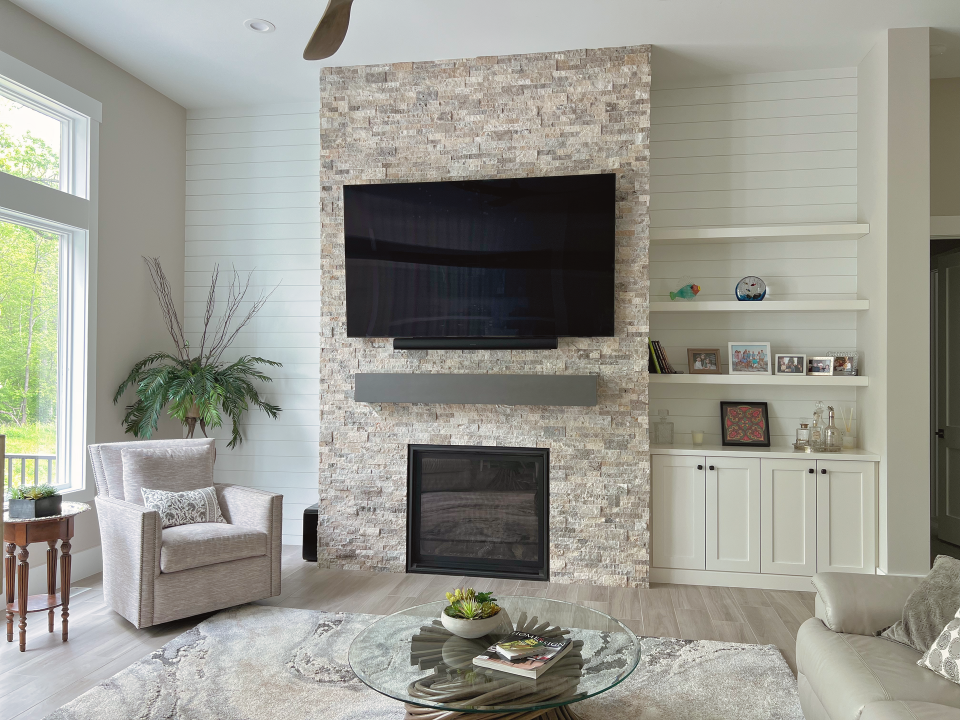 Living room with fireplace, TV, built-in shelves, and a seated armchair. White, gray, and neutral tones.