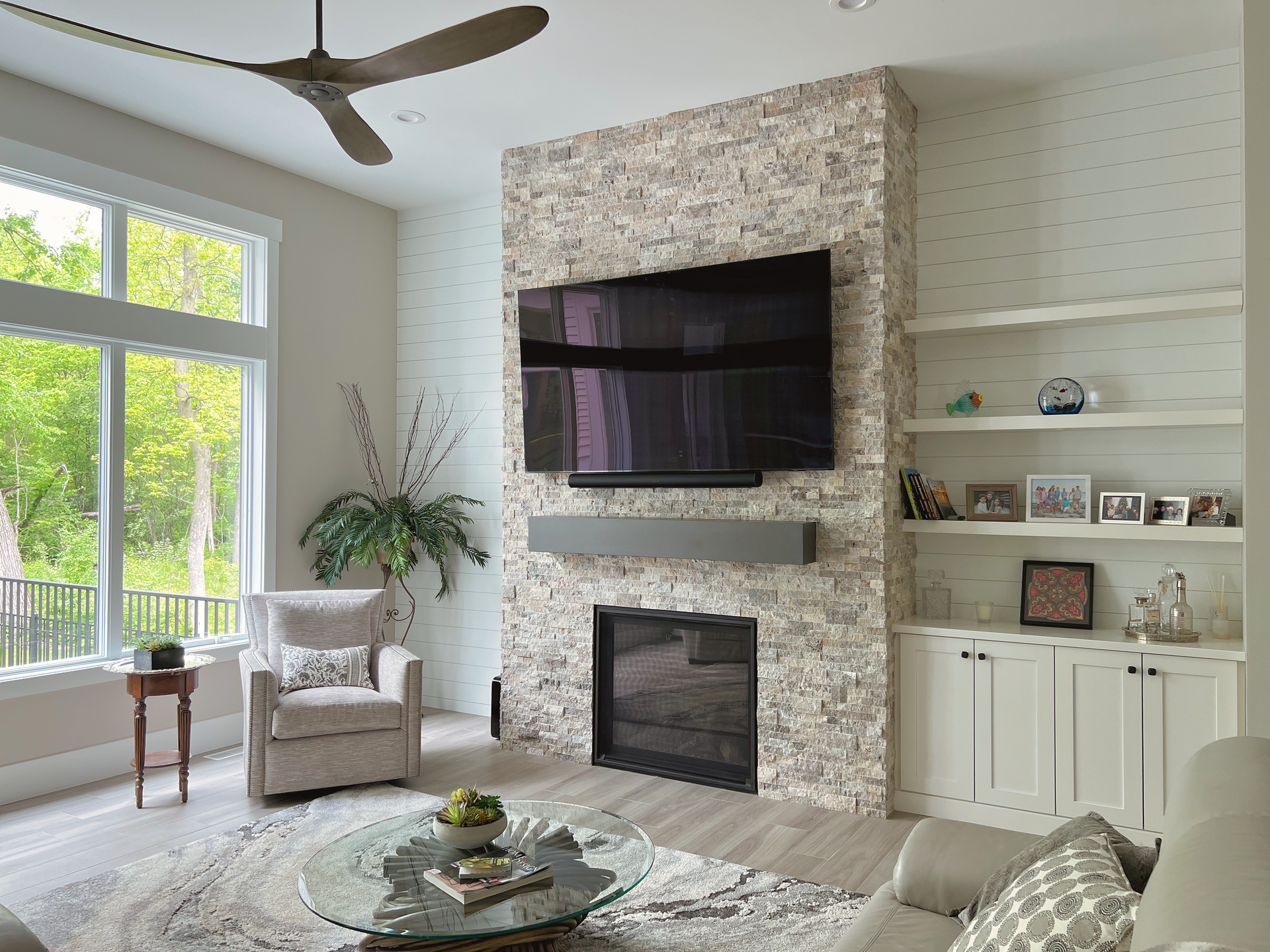 Living room with fireplace, TV, built-in shelves, armchair, large window with trees, and a coffee table.