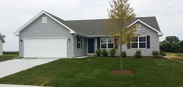 Gray house with a white garage door, surrounded by green grass and a small tree.