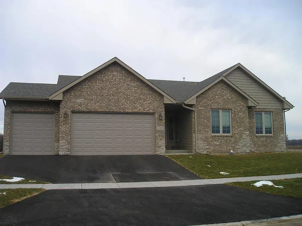 Brick house with two-car garage and driveway on a cloudy day.