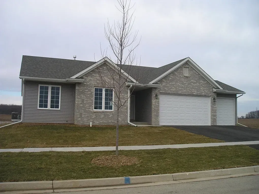 Brick and siding house with a two-car garage, small tree, and cloudy sky.