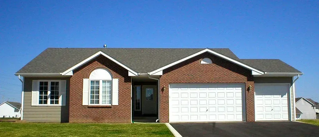 Brick house with white garage doors, windows, and a dark gray roof against a blue sky.