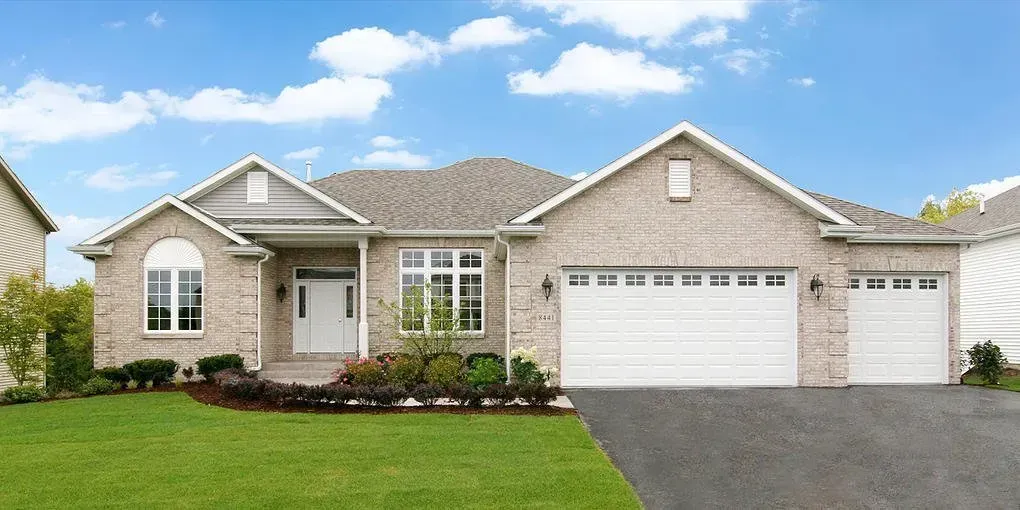 A brick house with a white garage and a green lawn under a blue sky.