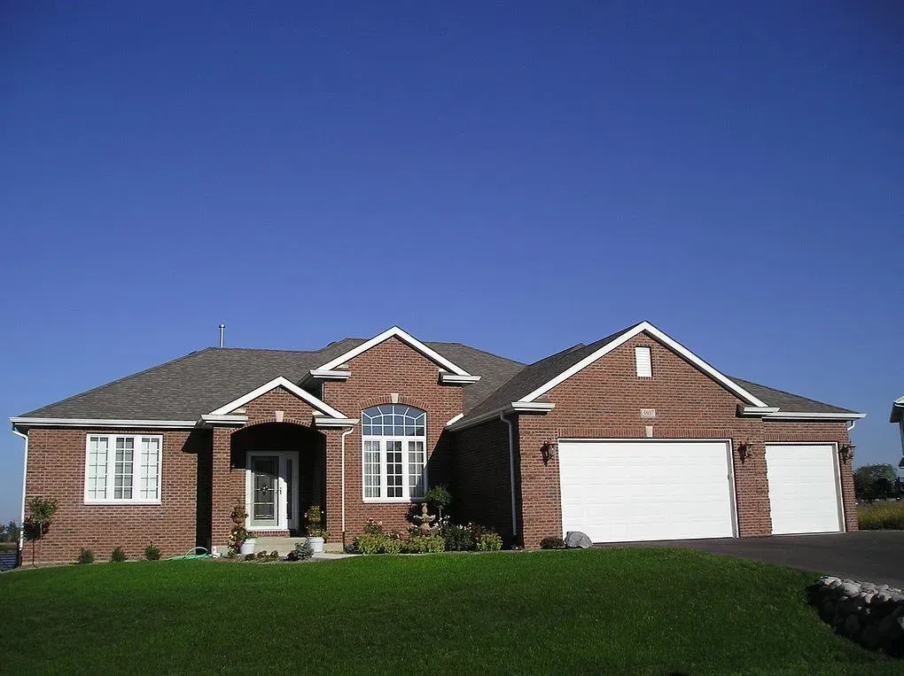 Brick house with two-car garage and manicured lawn under a clear, blue sky.