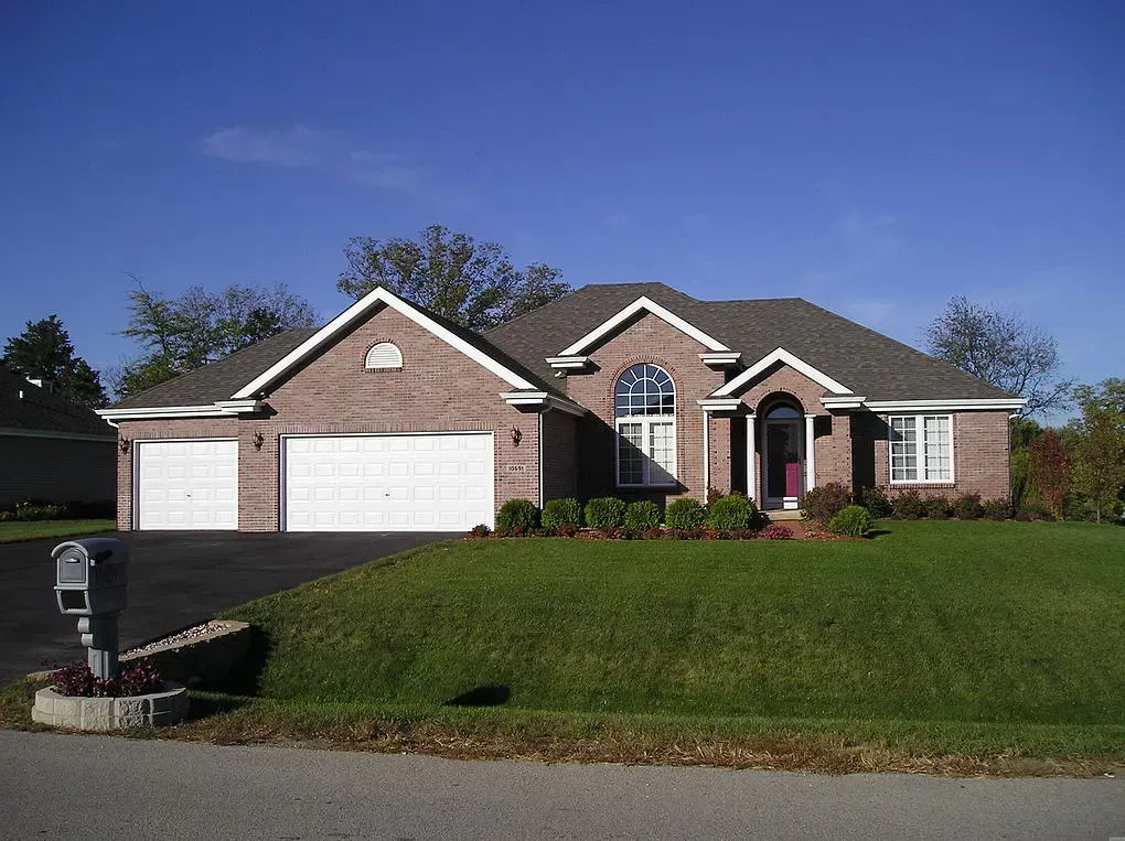 Brick ranch home with two-car garage, arched front window, green lawn, and blue sky.