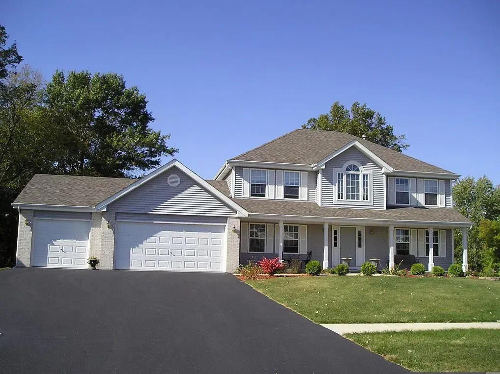 Two-story gray house with a driveway, attached garage, and a green lawn under a blue sky.