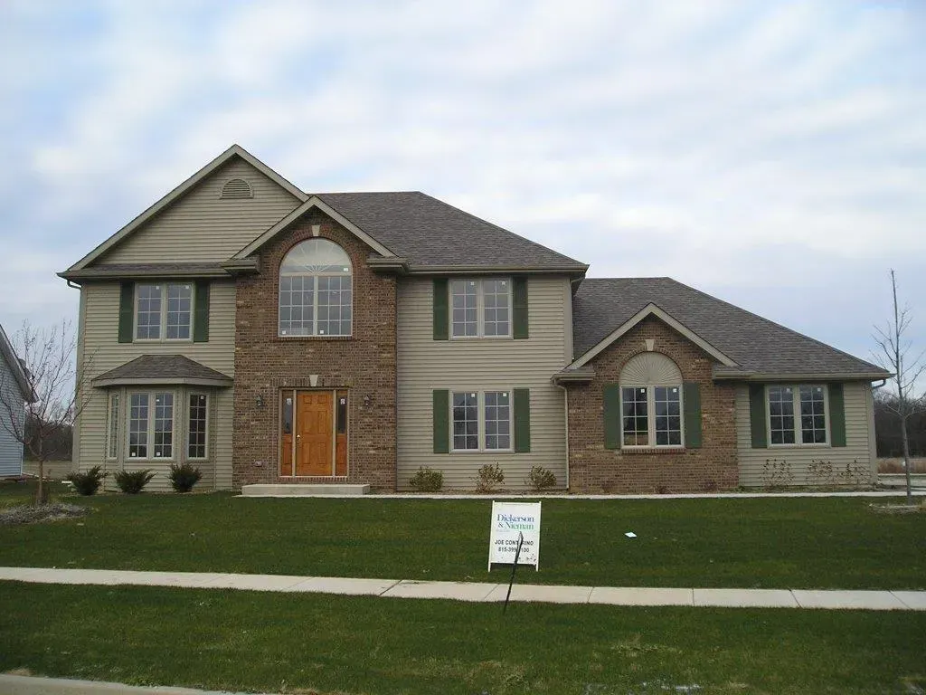 Two-story house with brick and tan siding, green shutters, brown roof, and an orange front door.