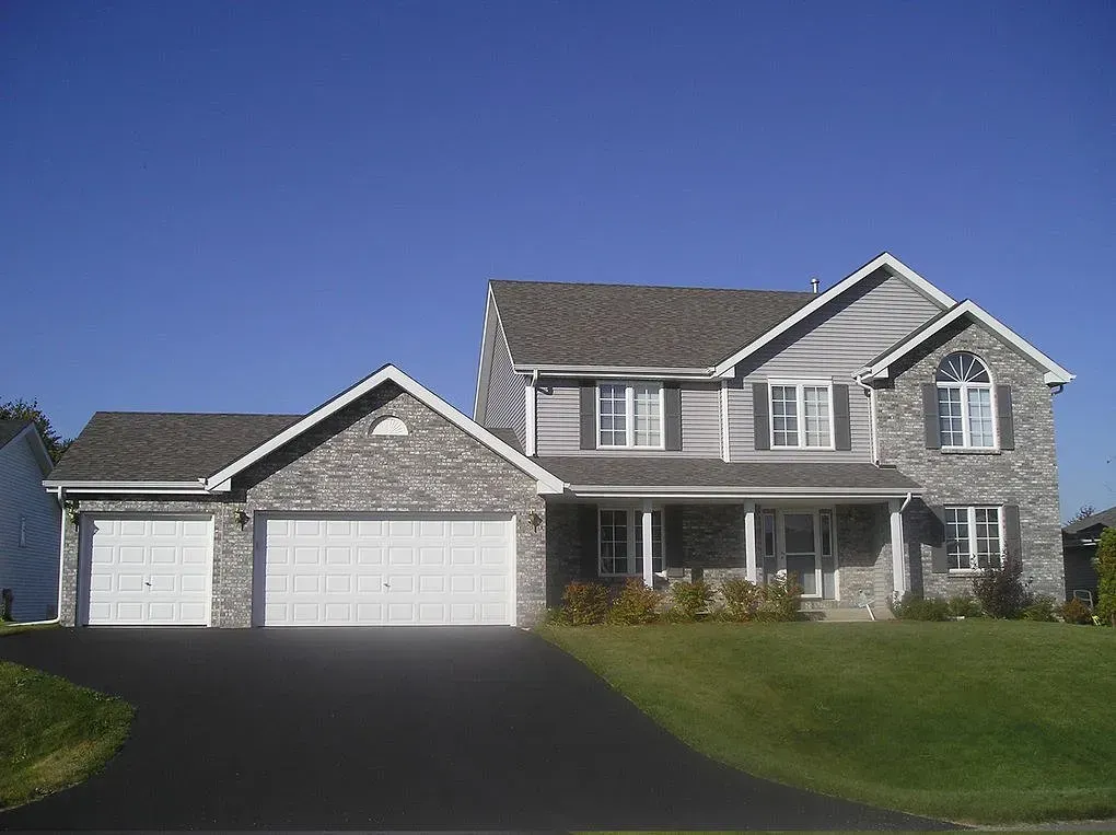 Two-story house with gray siding and stone accents, two-car garage, green lawn, and blue sky.