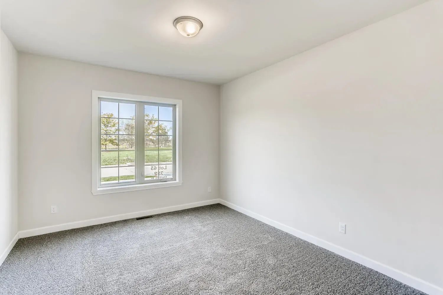 Empty room with gray carpet, white walls, a window, and a ceiling light.