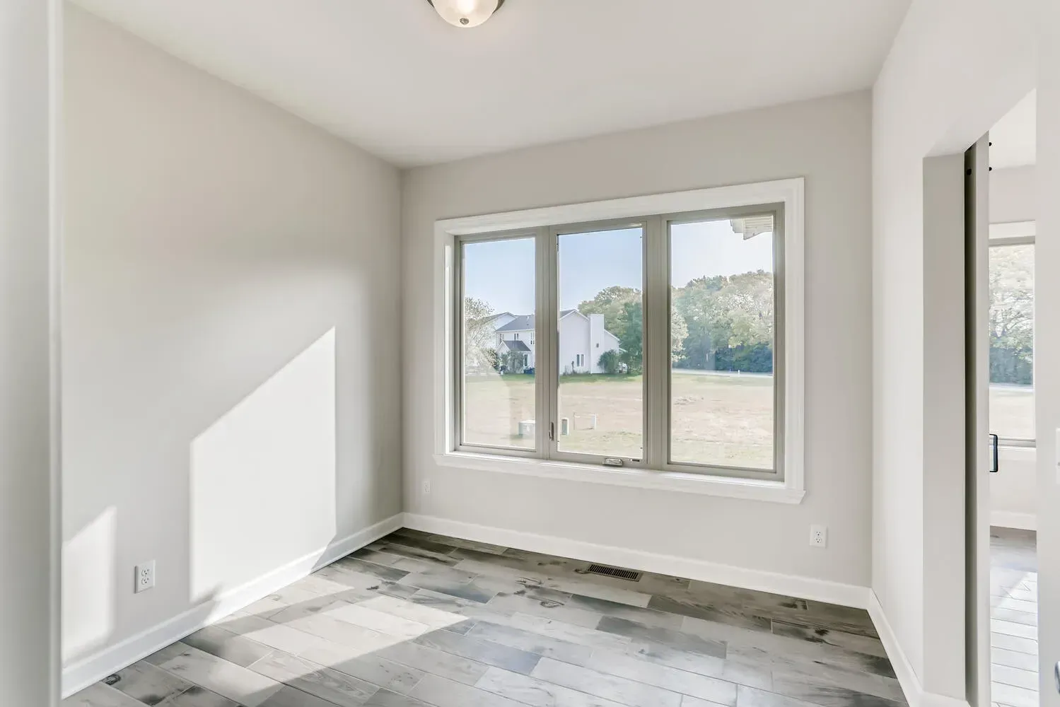 Empty room with large window, grey walls and flooring, door on right.