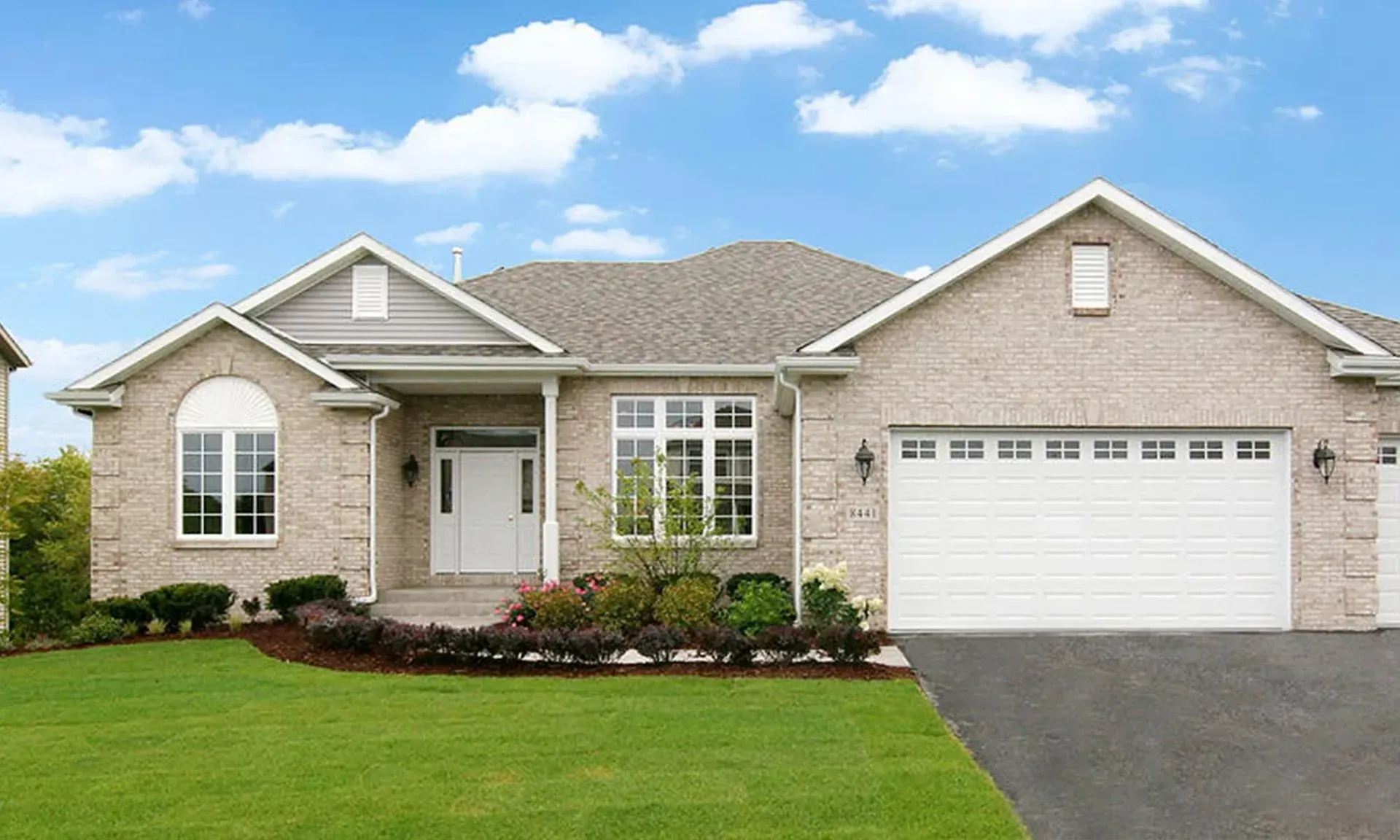 Suburban home with light brick exterior, green lawn, and blue sky.