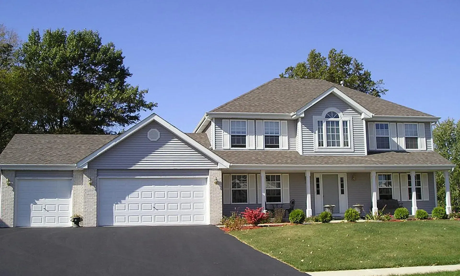 Gray two-story house with a two-car garage, porch, and driveway on a sunny day.