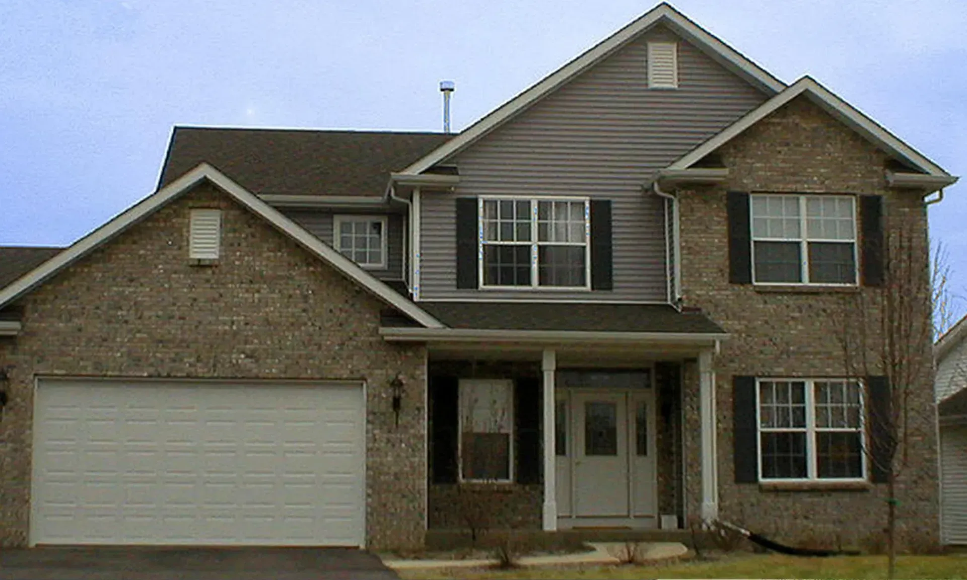 Two-story brick house with a garage and black shutters under a cloudy sky.