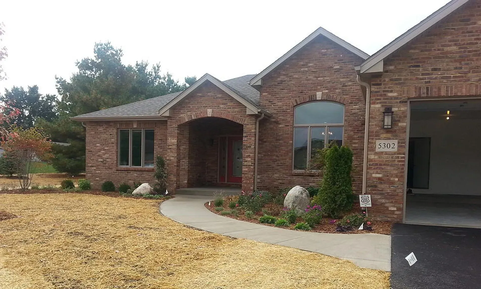 Brick ranch house with a garage, arched entryway, and landscaping on a brown lawn.