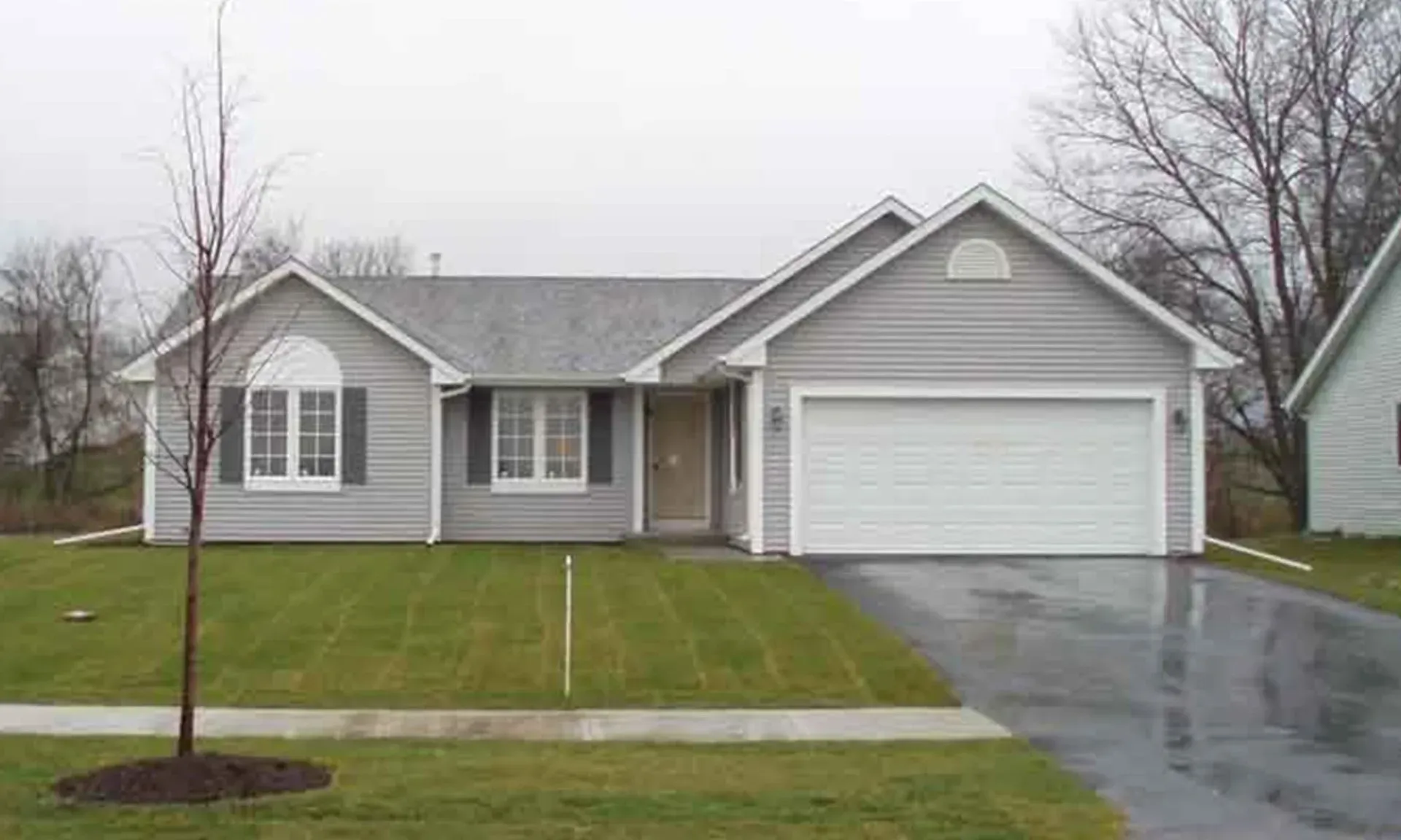Gray house with attached garage, green lawn, cloudy sky.