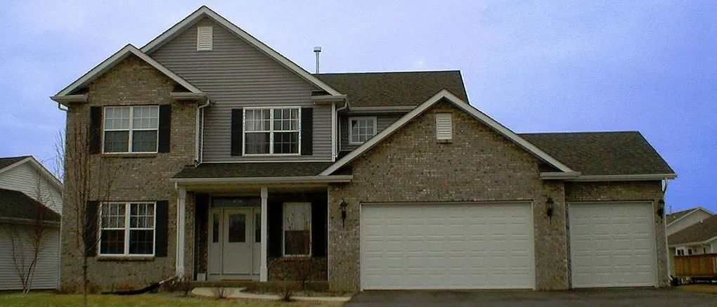 Two-story brick house with a two-car garage, front porch, and blue sky background.