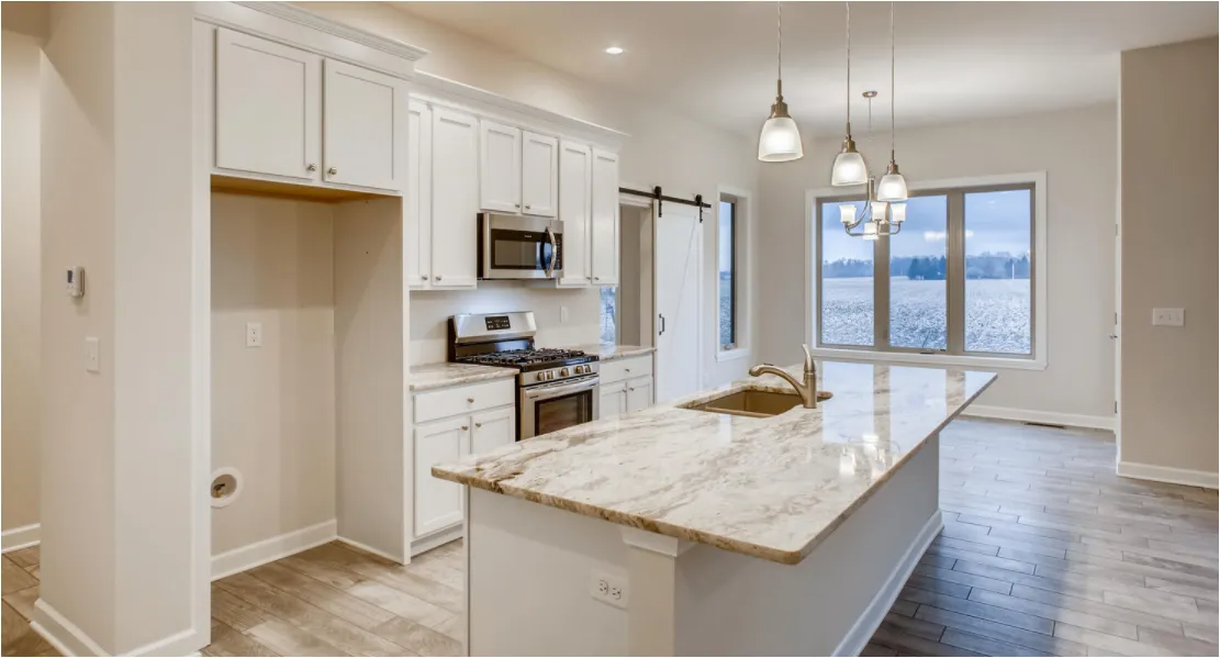 Modern kitchen with white cabinets, granite island, and large windows overlooking water.