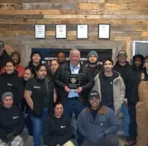 A group of people standing together indoors against a wood-paneled wall, with one person holding an award in the center.