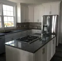 A modern kitchen with white cabinets, dark granite countertops, a center island with a gas cooktop, and stainless fridge.