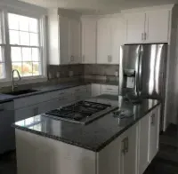 A modern kitchen with white cabinets, dark granite countertops, a center island with a gas cooktop, and stainless fridge.