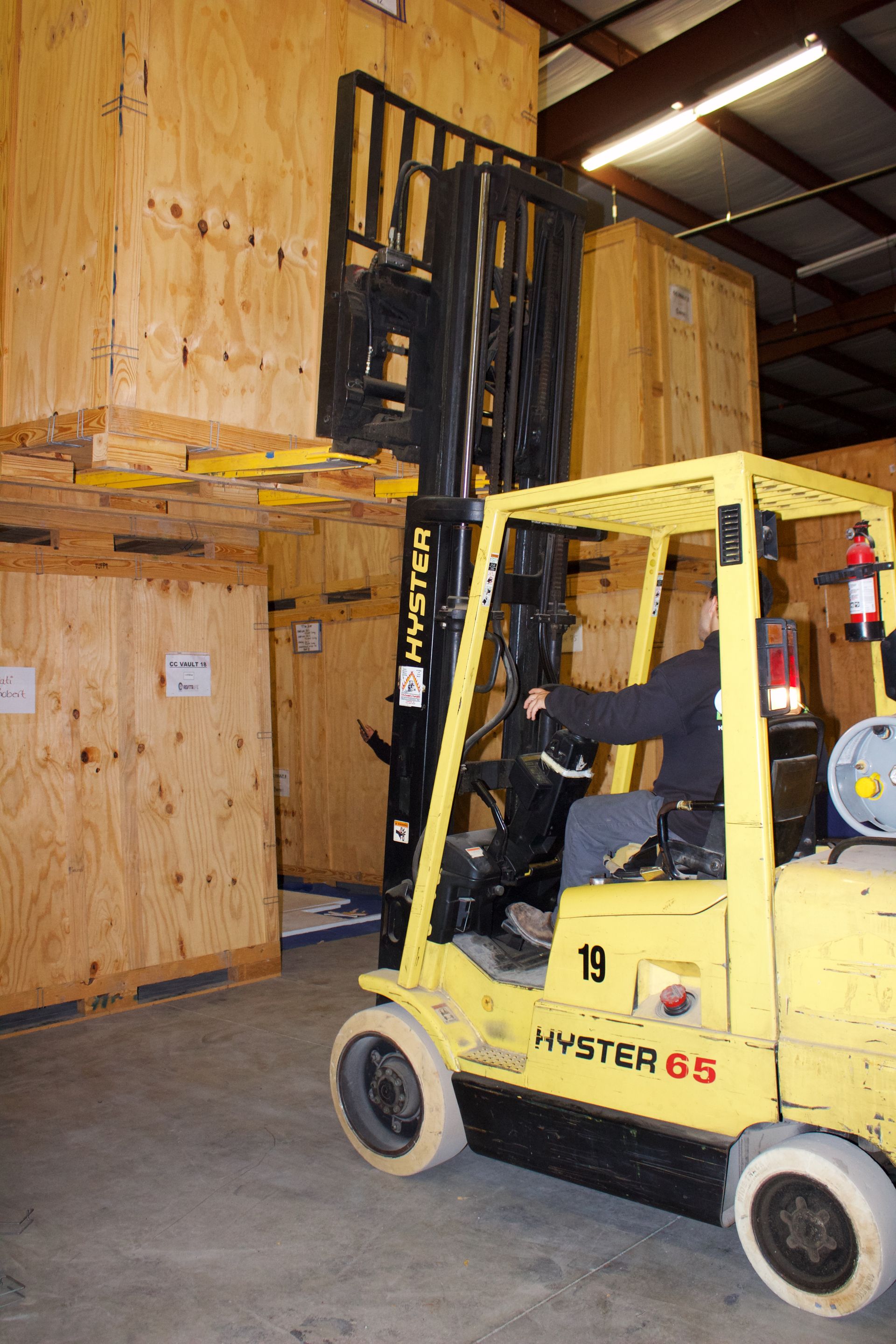 A forklift operator in a warehouse moves a large wooden shipping crate stacked on top of another.