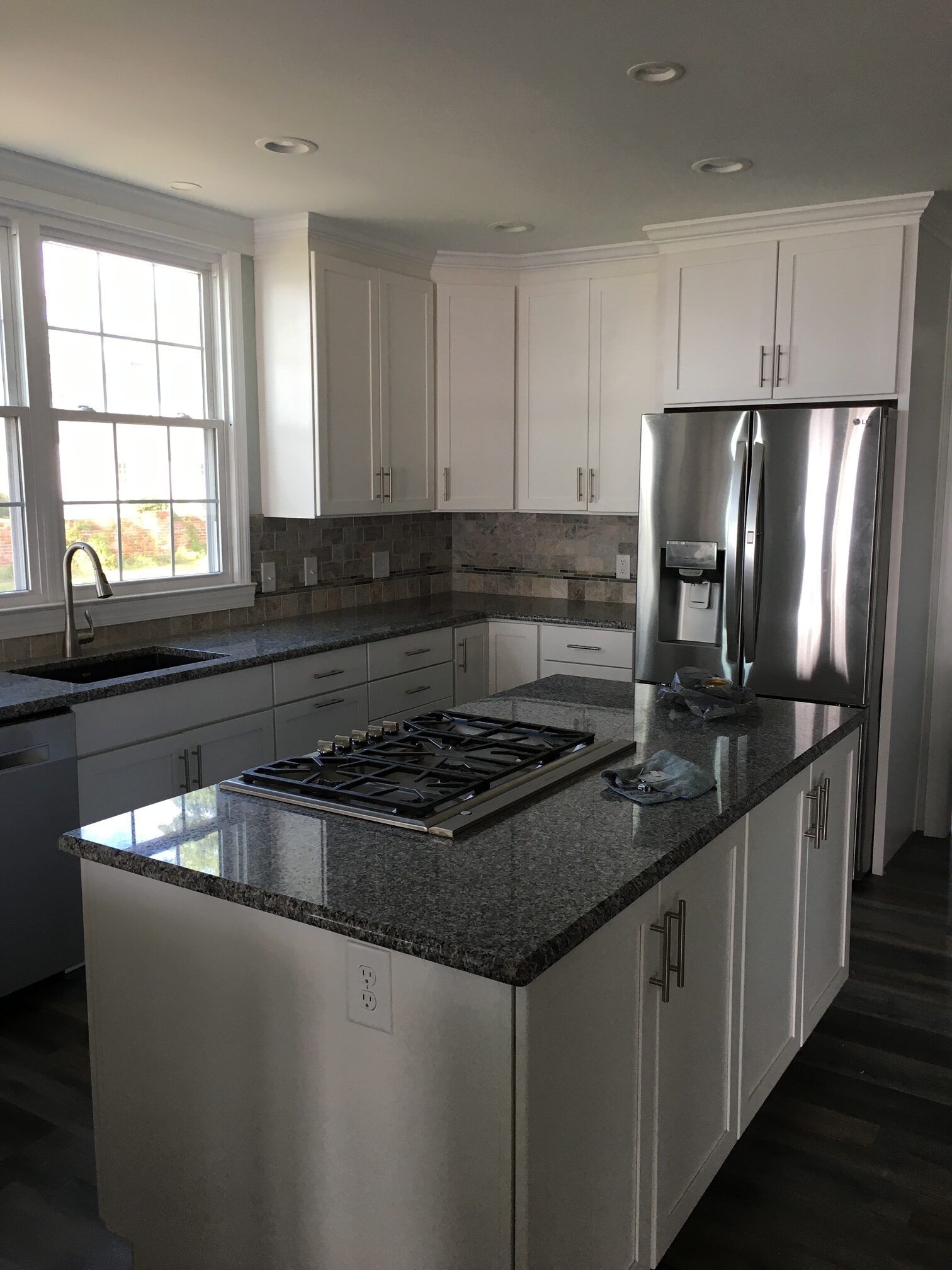 A modern kitchen with white cabinets, dark granite countertops, a center island with a gas cooktop, and stainless fridge.